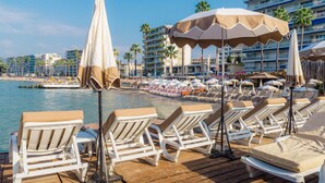 A beachside resort with sun loungers, umbrellas, and a view of the sea and hotel buildings.
