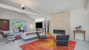 A modern living room with a white sofa, black chairs, a red rug, a fireplace, and a TV.