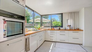 A modern kitchen with a built-in oven, white cabinetry, a large window, and a view of the outdoors.