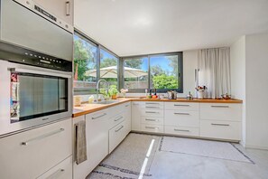 A modern kitchen with a built-in oven, white cabinetry, a large window, and a view of the outdoors.