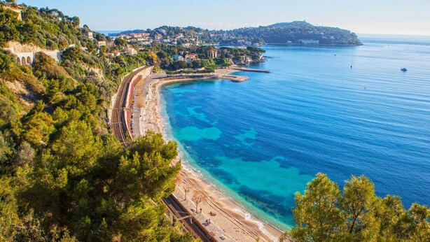 A coastal town with a beach, a train track, and a mountainous backdrop.