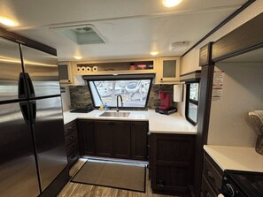 A compact kitchen with a stainless steel refrigerator, a sink, and a coffee maker. - Mountain Shadows RV & MHC (Draper)