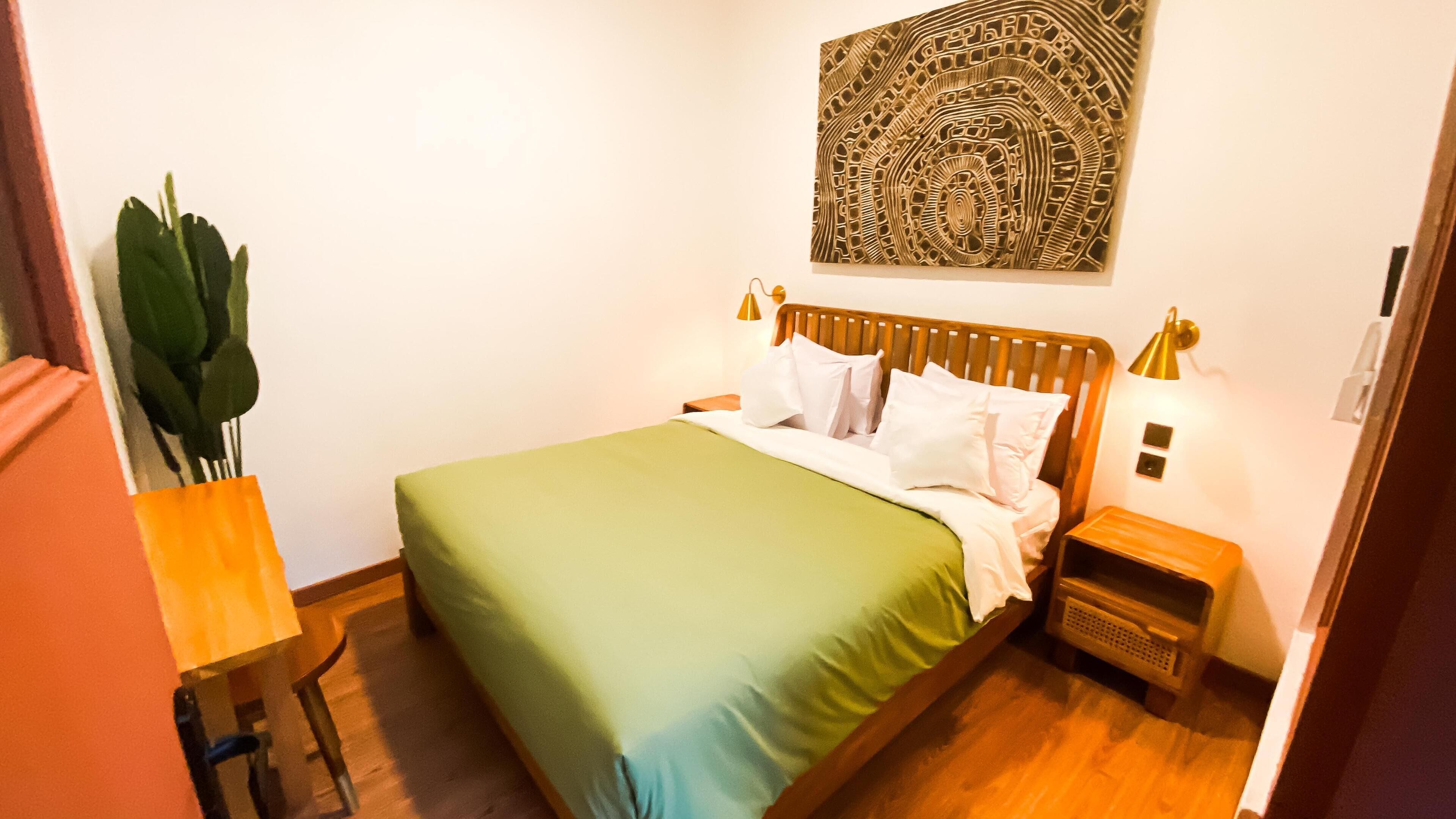 Een netjes ingerichte slaapkamer met een bed, nachtkastjes, een kunstwerk aan de muur en een potplant.