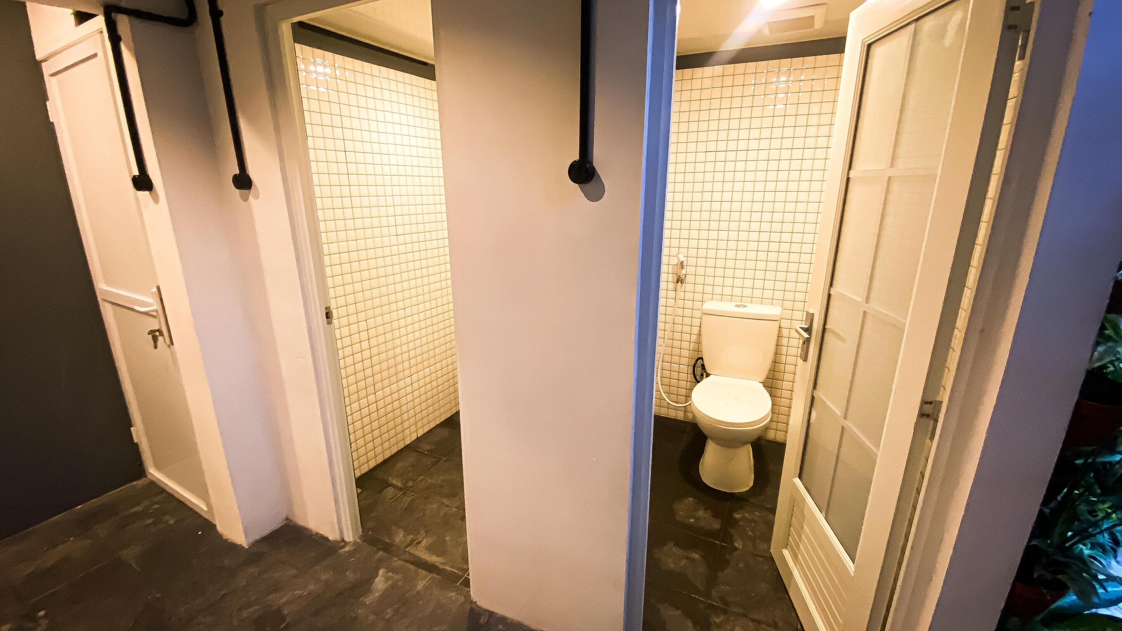 Un couloir étroit avec un mur recouvert de carreaux et des toilettes visibles au fond.