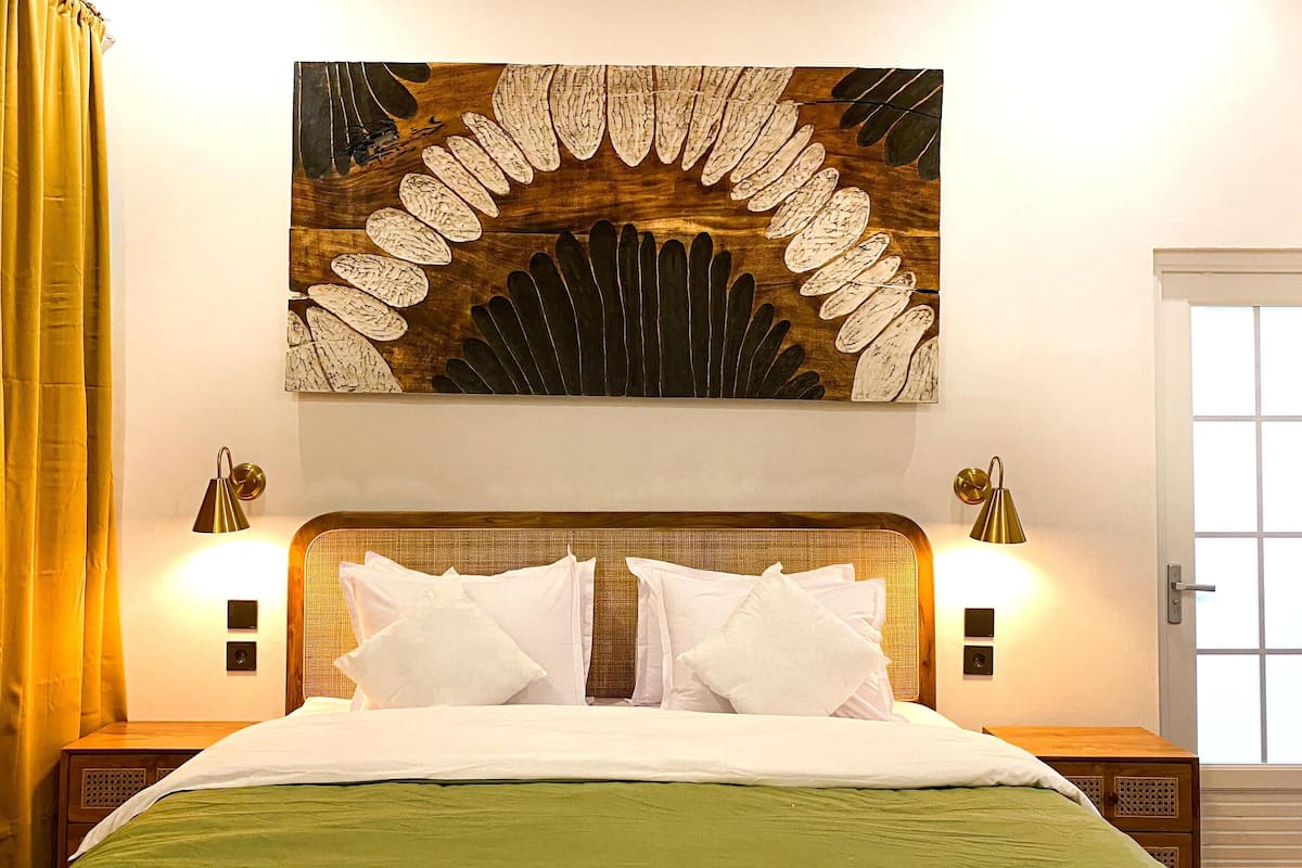Une chambre d’hôtel avec un grand lit, deux lampes de chevet, une œuvre d’art accrochée au mur et une fenêtre avec des rideaux.