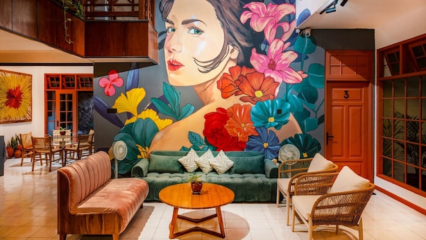 Un vaste espace de vie agrémenté d’une grande fresque florale, d’un canapé vert, d’une table basse en bois, de fauteuils en osier et d’un ensemble de salle à manger.