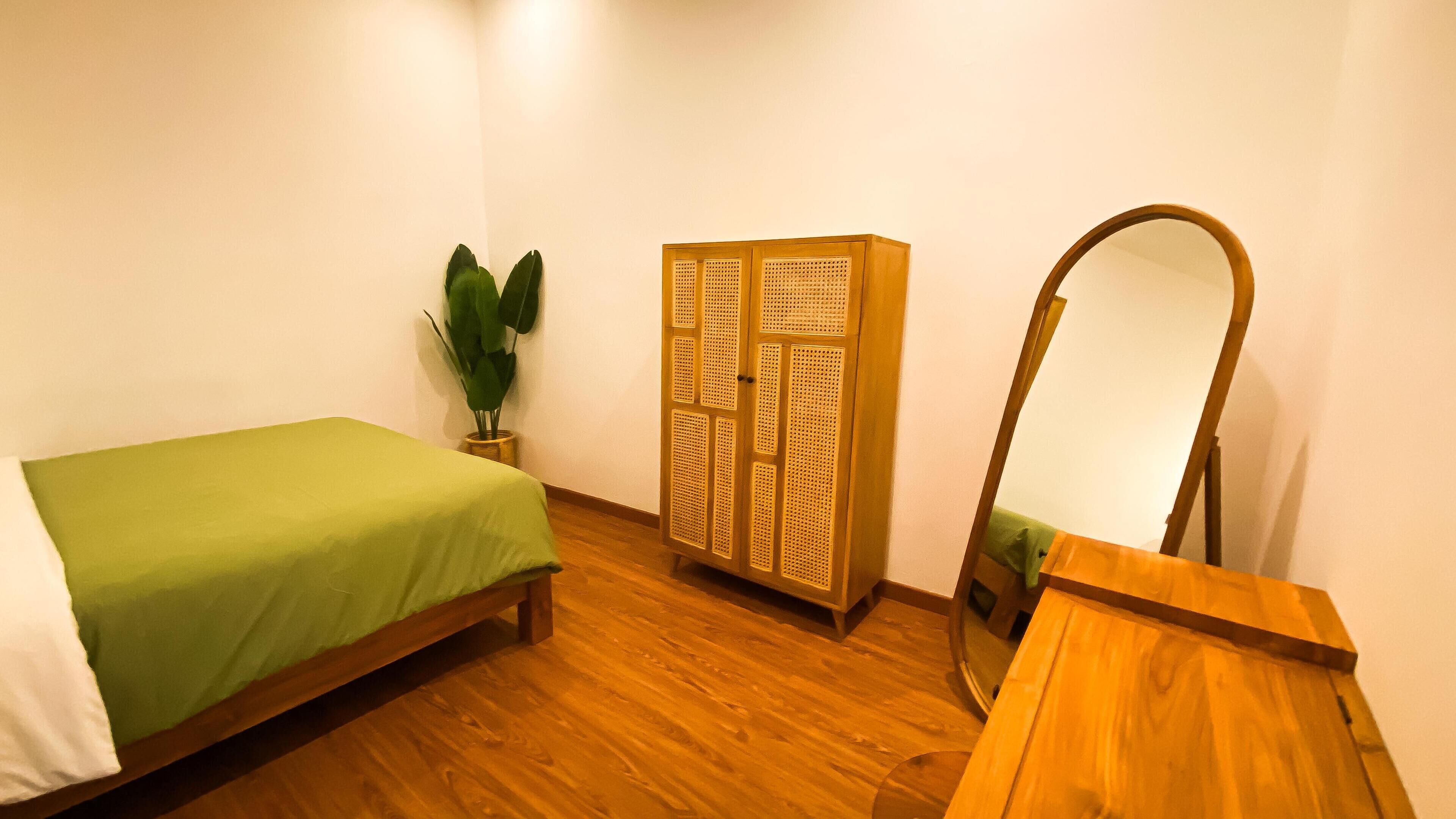 A bedroom with a bed, a wardrobe, a mirror, and a potted plant.