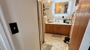 A narrow hallway leading to a bathroom with patterned flooring, a sink, and a mirror.