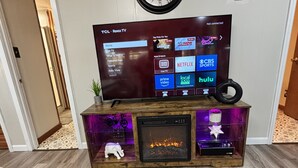 A living room with a TV on a wooden stand, a fireplace, and a clock on the wall.