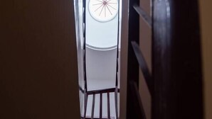 Un couloir étroit et sombre, avec une rambarde métallique d’un côté et une porte blanche au fond.