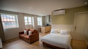 Ein modernes Hotelzimmer mit einem Bett, einer Couch, einer Küchenzeile und großen Fenstern.