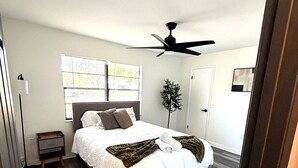Une chambre à coucher avec un lit, un ventilateur de plafond, une fenêtre avec des stores et une porte.
