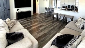 Un salon moderne doté d’un téléviseur à écran plat, d’un ventilateur de plafond et d’un coin repas avec une cuisine en arrière-plan.