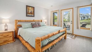 A bedroom with a wooden bed frame, a nightstand, a lamp, and a painting on the wall. - Hot Tub, King Beds, Mountain Views on Balcony & Patio (Estes Park)
