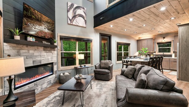 Una sala de estar moderna con chimenea de piedra, un sofá gris cómodo y un comedor con cocina al fondo.