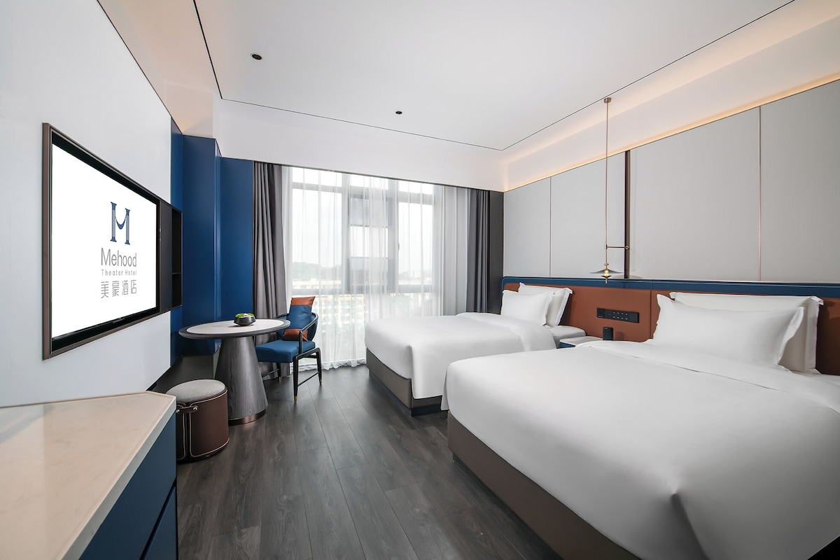 A hotel room with two beds, a small table, a chair, and a TV mounted on the wall.
