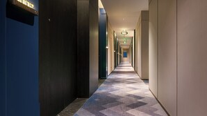 Um corredor comprido e estreito com carpete estampado, paredes de madeira e uma placa à esquerda.