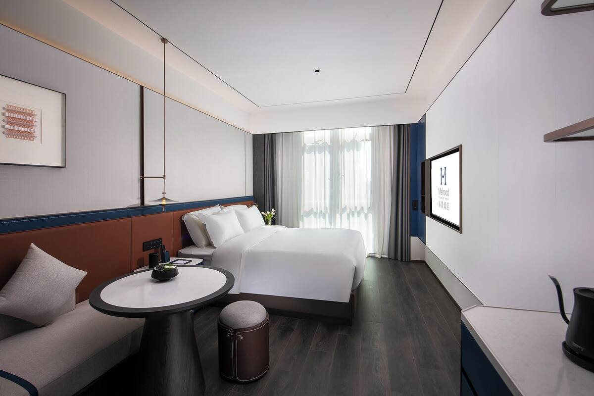 Habitación de hotel moderna con una cama grande, una mesa redonda, un sofá y vistas al exterior.