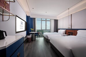 Ein Hotelzimmer mit Bett, Schreibtisch, Stuhl, einem kleinen Tisch mit Vase und einem großen Fenster mit Blick auf die Stadt.