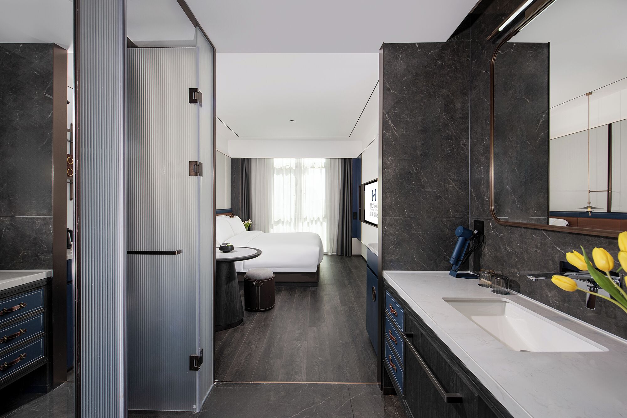 A modern hotel room with a large bed, a separate sitting area, a bathroom with a large mirror, and a sink.
