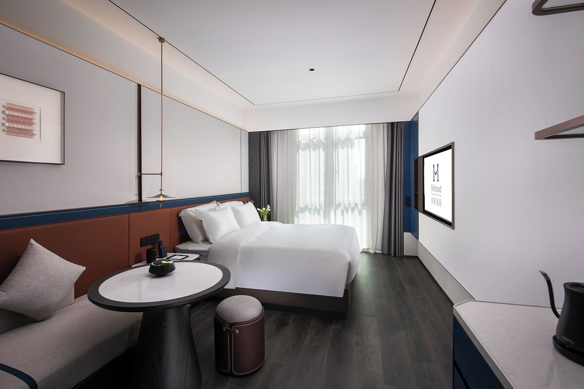 Habitación de hotel moderna con una cama grande, una mesa redonda, un sofá y vistas al exterior.