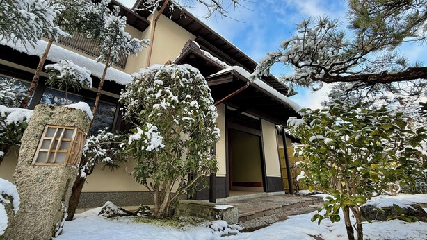 Un bâtiment traditionnel avec une porte en bois, une lanterne en pierre et des arbres couverts de neige.