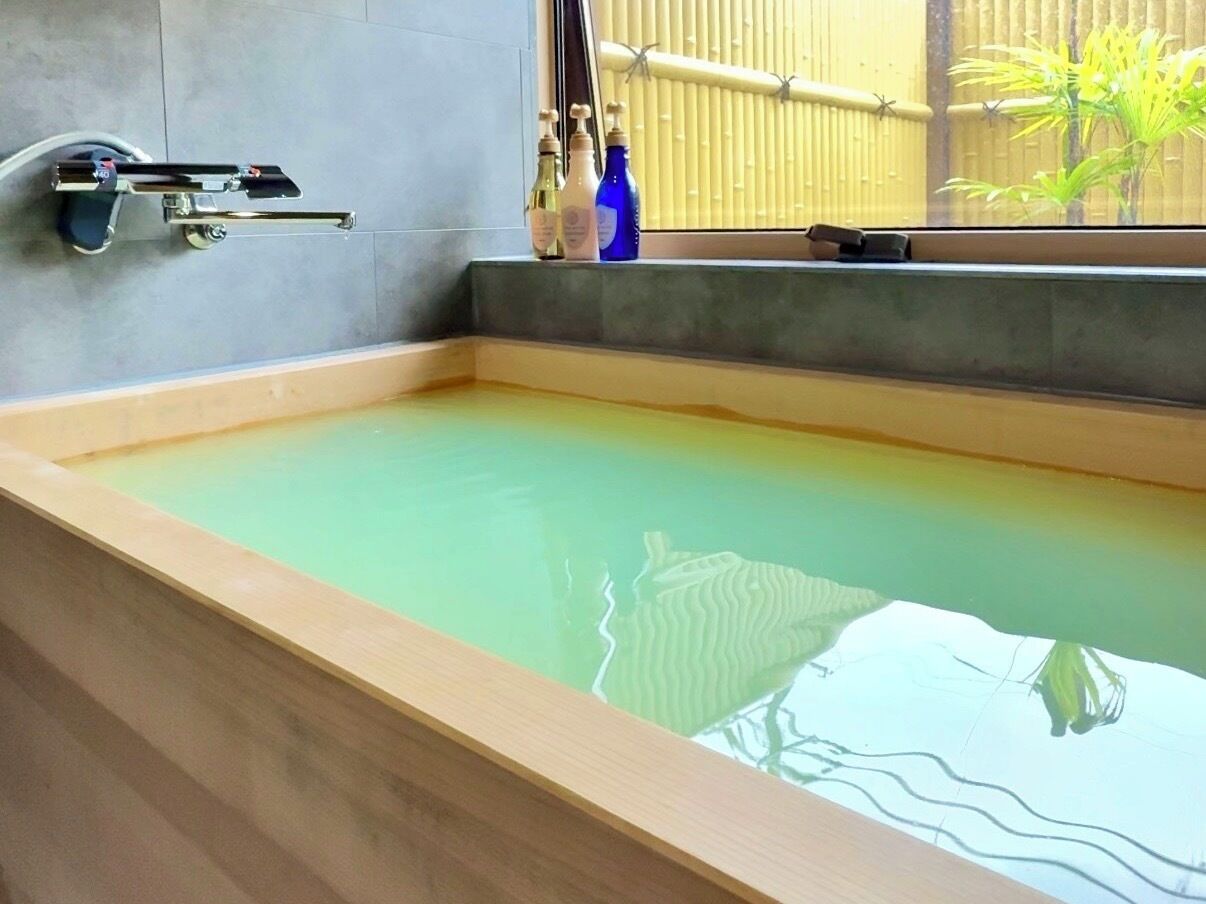 Una bañera con borde de madera, una ventana con persianas y un estante con botellas.