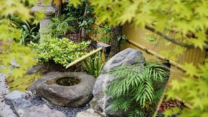 Un jardin agrémenté d’une fontaine en pierre, d’une clôture en bambou et de diverses plantes.
