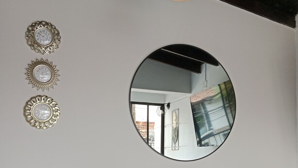 A grey sofa with a round mirror above it, a potted plant, and three wall-mounted decorative clocks. - Envigado: Tradición y Modernidad (Envigado)