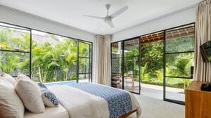 Camera da letto con un letto, una ventola a soffitto, ampie finestre e vista sul verde.