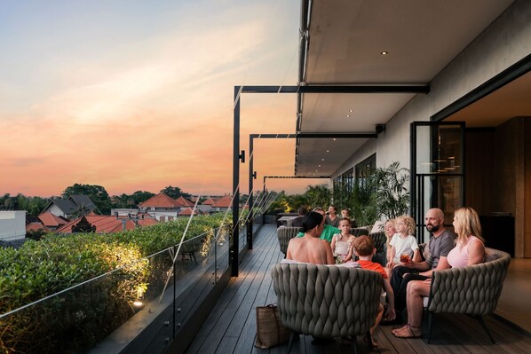 A rooftop terrace with a group of people seated on cushioned chairs, overlooking a cityscape during sunset. - Anwa Bali Boutique Resort (Keroboken Kelod)