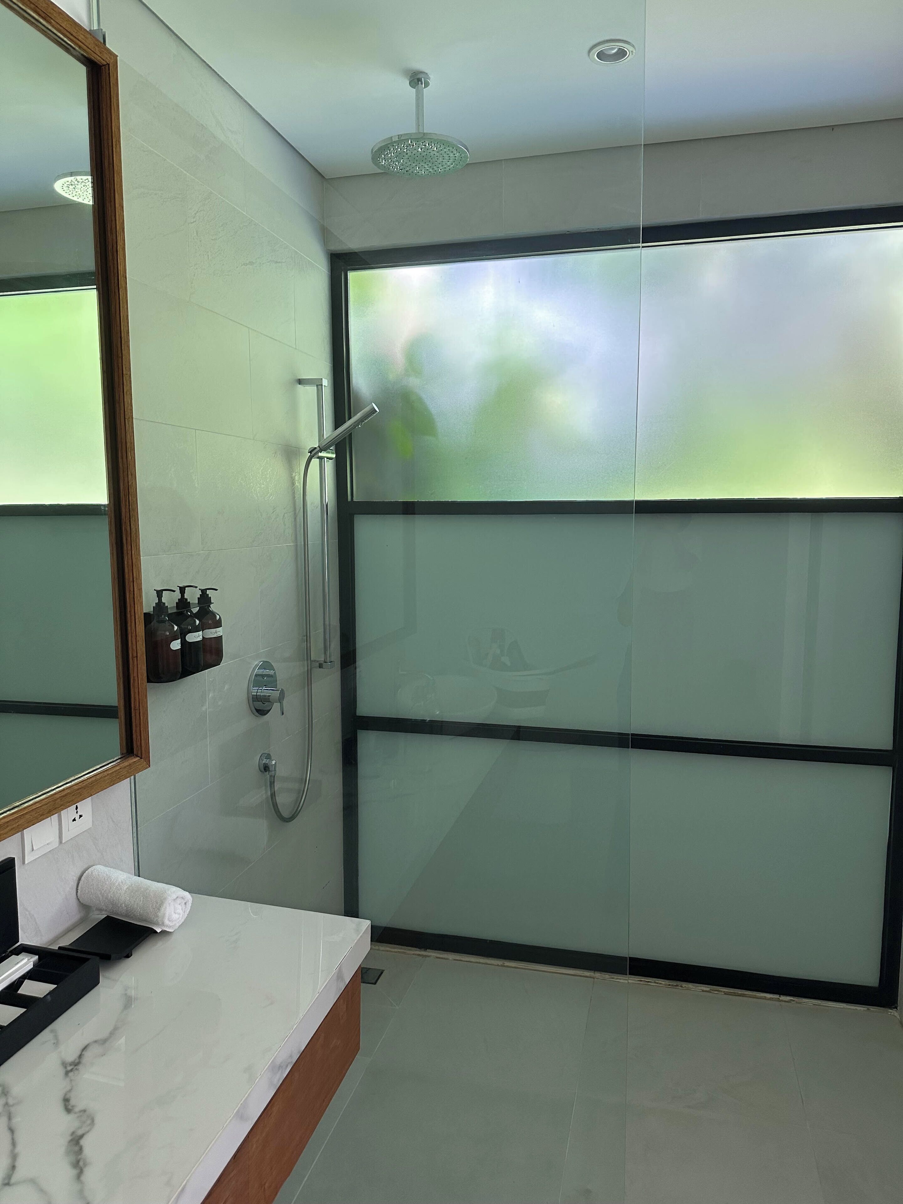 A modern bathroom with a glass shower enclosure, a marble sink, and a large mirror.