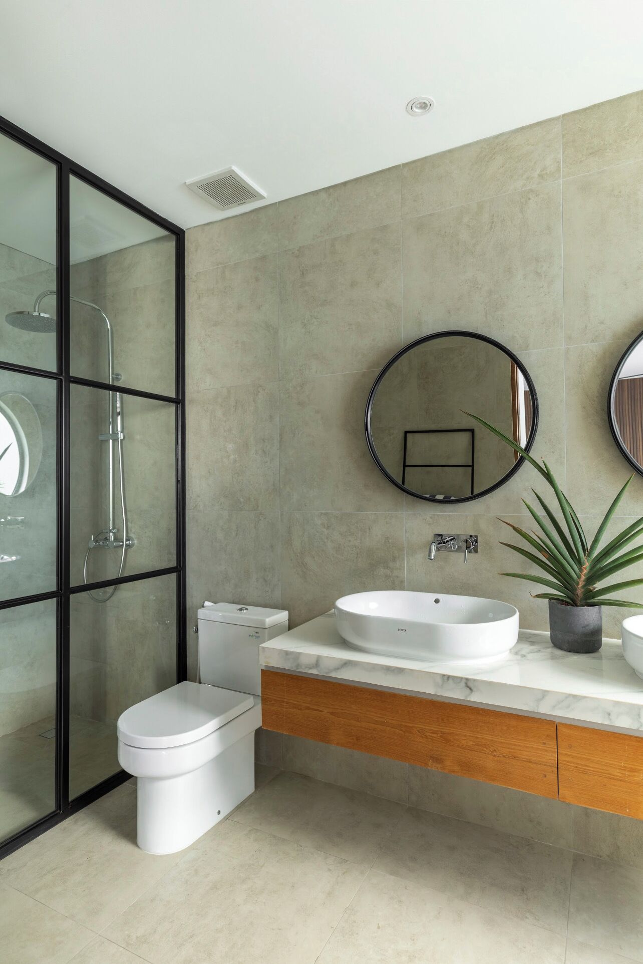 Un baño moderno con ducha de vidrio, inodoro, tocador con lavamanos y espejo.