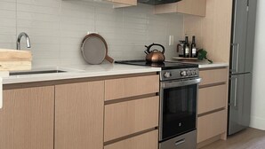 Une cuisine moderne avec des meubles de couleur bois clair, un réfrigérateur en acier inoxydable, un four et une bouilloire posée sur le plan de travail.
