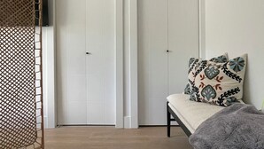 Une pièce comprenant un lit, un banc, un téléviseur et deux portes.