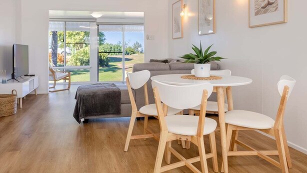 A modern living room with a round dining table, white chairs, a grey sofa, and a TV on a white stand. - Welcome to - Family Tides! (Mulambin)