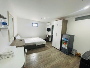 A compact hotel room with a bed, a desk, a wardrobe, and a refrigerator. - Royal Hotel & Apartment (Da Nang)