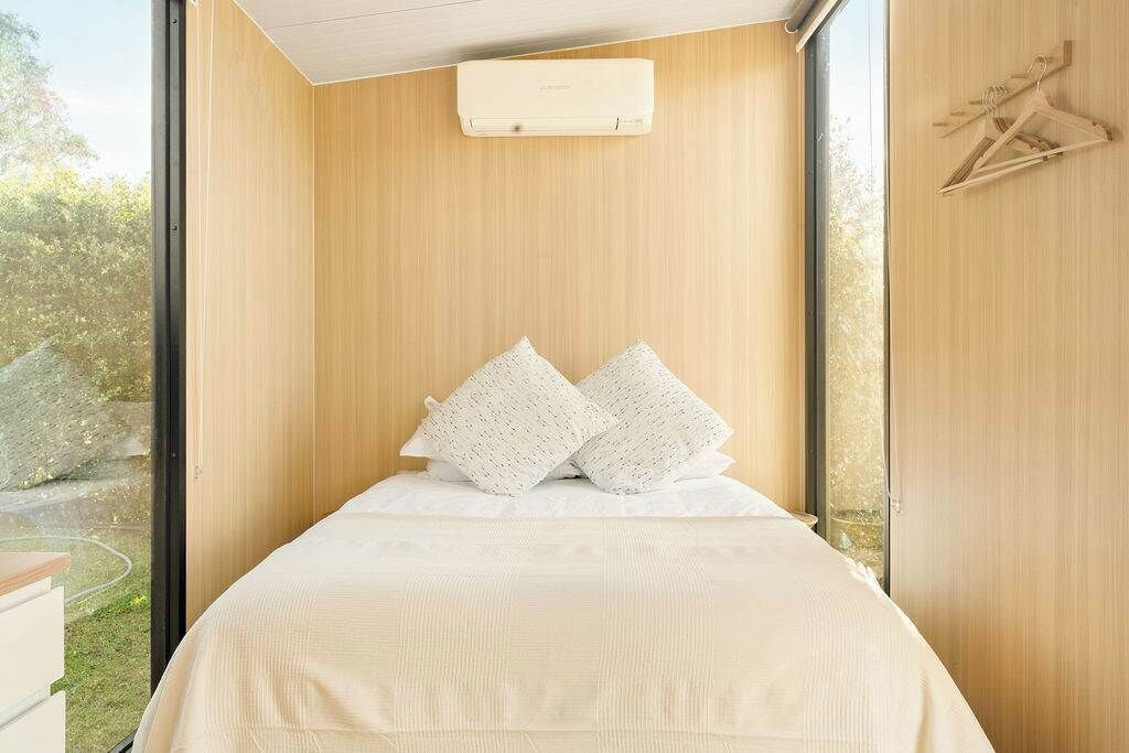 A modern bedroom with a large window, a bed with white linens, and a wall-mounted air conditioner.