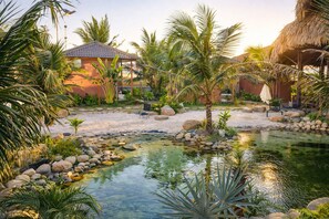 A tropical garden with a pond, palm trees, and a thatched-roof structure. - Melaka Ho Tram - Beachside Bungalows (Ho Chi Minh City)