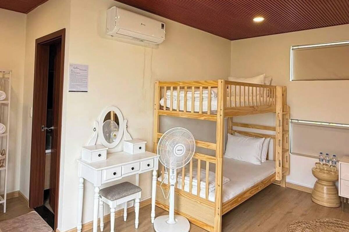 Une chambre avec un lit superposé, une coiffeuse avec un miroir, un bureau et un ventilateur sur pied.