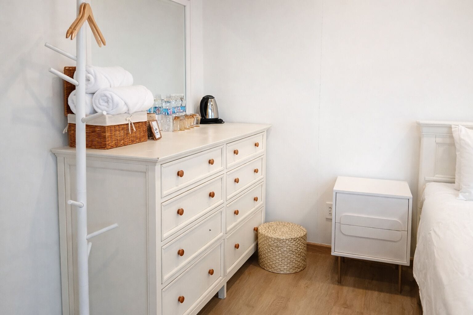 A white dresser with multiple drawers, a wicker basket, and a mirror.