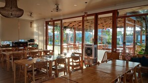 Een restaurant met houten tafels en stoelen, grote ramen en uitzicht op buiten.