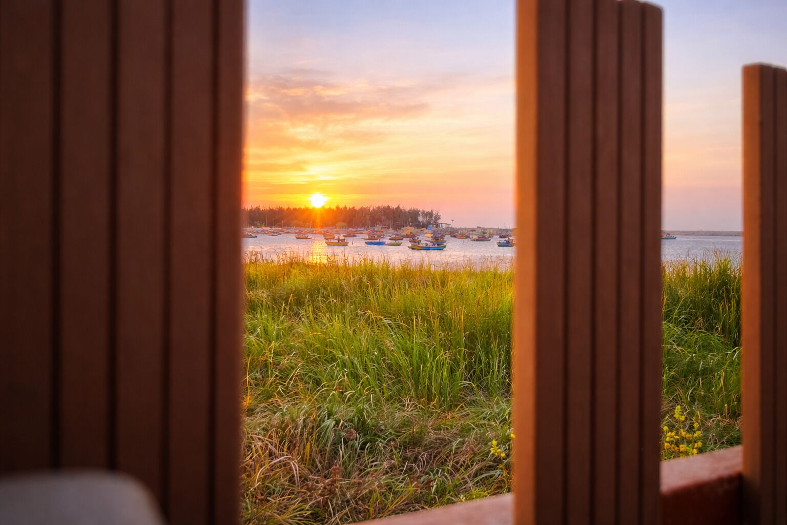 Vista a través de un marco de madera de un atardecer sobre un cuerpo de agua con barcos.