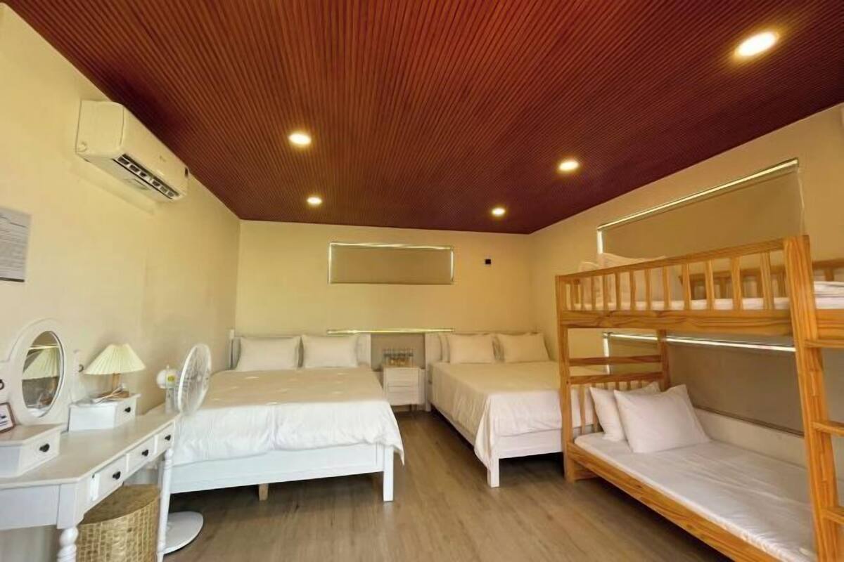 Une chambre avec des lits superposés, une table de chevet avec une lampe, un miroir et un ventilateur de plafond.