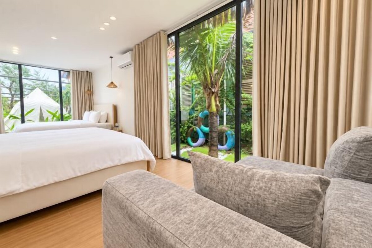 A bedroom with a large bed, a sofa, and a view of outdoor greenery.