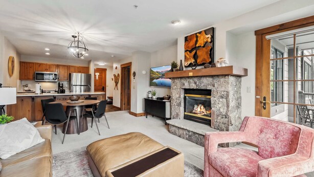 A modern living room with a fireplace, a dining area, and a kitchen with wooden cabinets and stainless steel appliances.