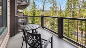 A balcony with a table and chairs, a railing, and a view of trees and a road.