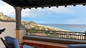 Un balcón con dos sillas azules, una mesita con fruta y vista a la playa y al océano.