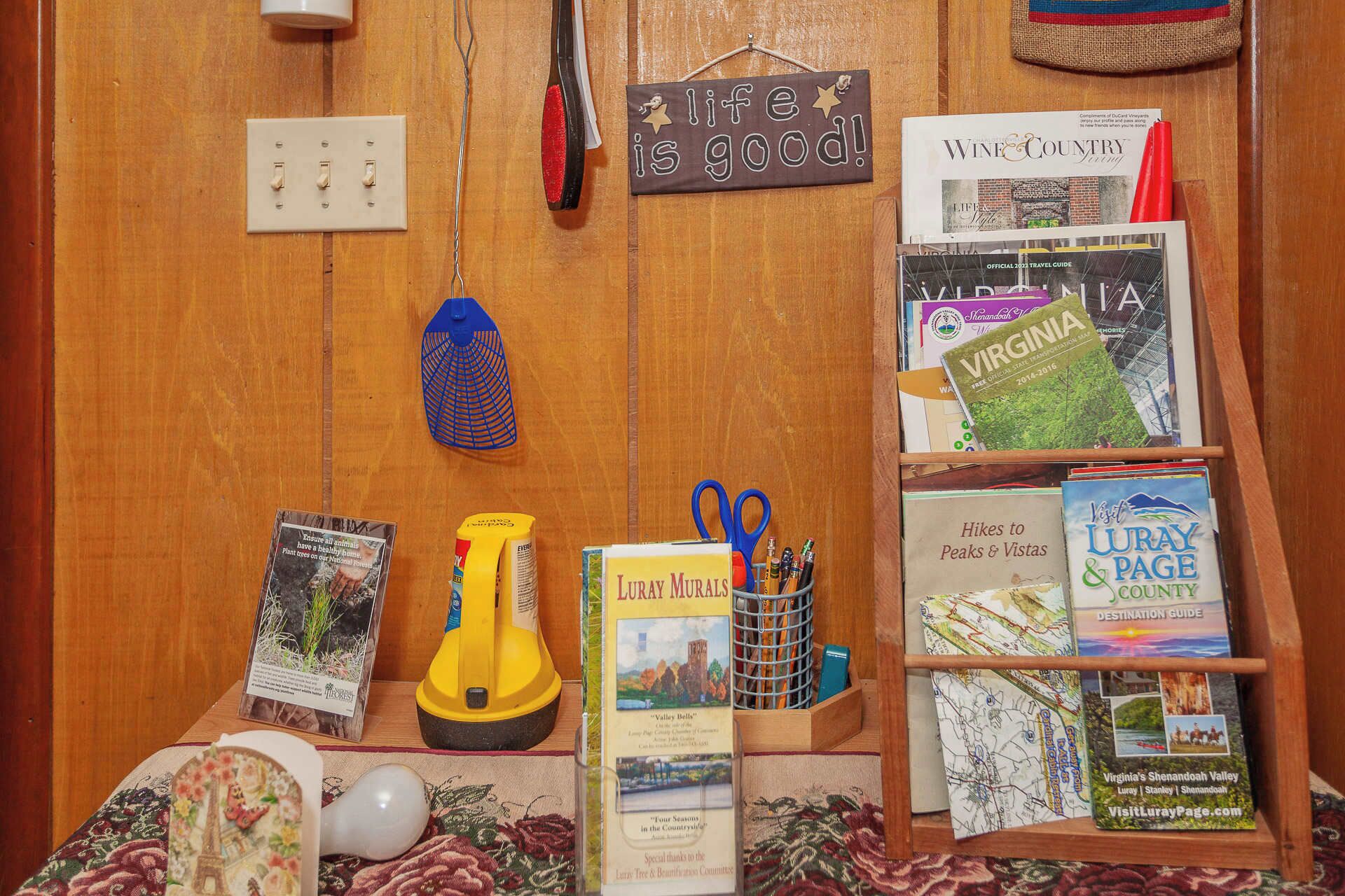 A wooden wall with a power outlet, a life is good sign, a magazine rack with travel guides, and a blue net.
