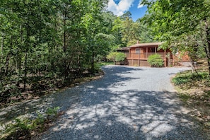 A wooden cabin with a gravel driveway surrounded by dense forest. - Private w Screened Porch, Deck & Dog-Friendly! (Luray)
